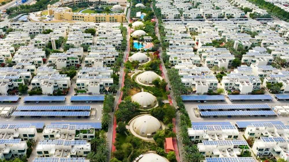Aerial view of a sustainable residential community in Abu Dhabi featuring solar powered homes, green spaces, tree lined walkways, and energy efficient urban planning.
