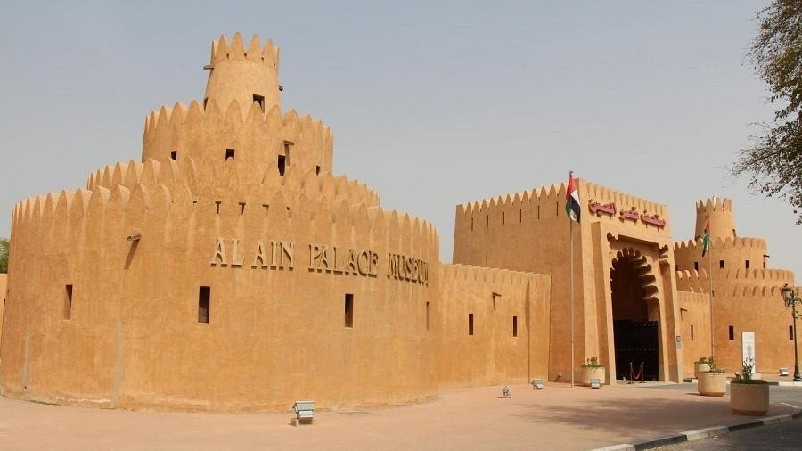 Exterior view of Al Ain Museum showing the traditional mud brick architecture, fortified walls, and the main entrance beside Al Ain Oasis in the UAE.