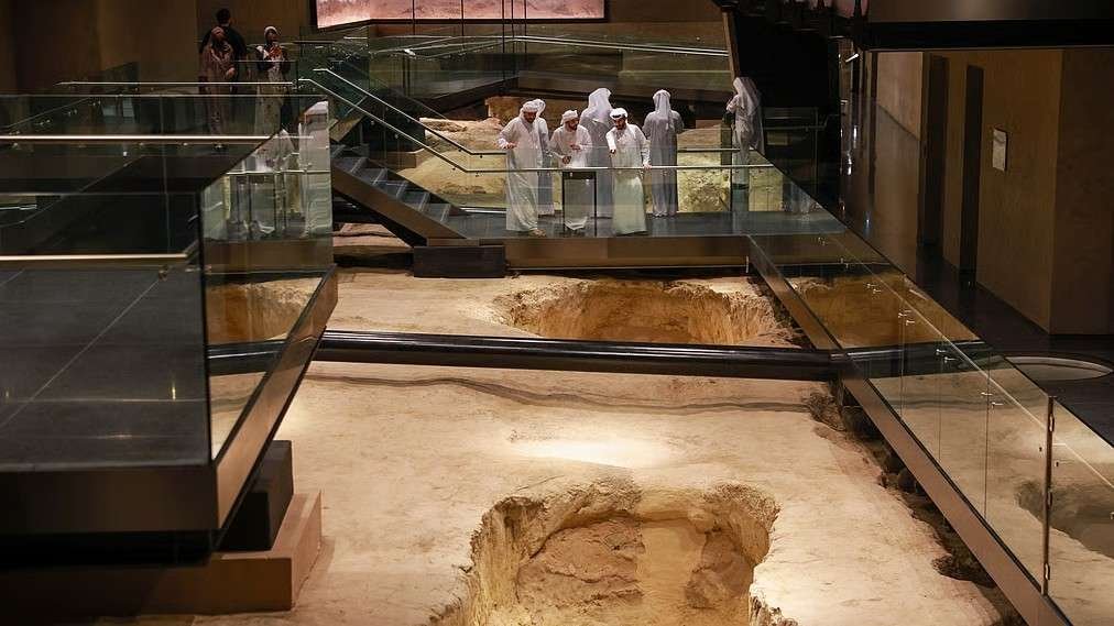 Interior view of Al Ain Museum featuring an archaeological excavation site, elevated walkways, and visitors exploring ancient artefacts and historical exhibits.
