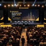 Audience attending Binance Blockchain Week 2026 at Dubai's Coca Cola Arena, with a large stage displaying Binance branding, the 2026 event dates, speaker seating, and hundreds of blockchain professionals gathered for the conference.