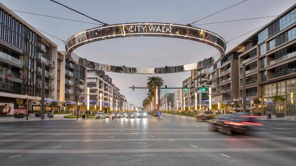 Illuminated City Walk Dubai entrance with its iconic circular sign, modern buildings, palm trees, and traffic at dusk in Dubai.