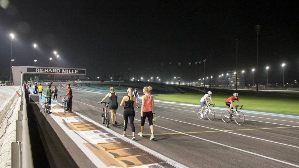 People cycling and walking during a free TrainYAS evening session at Yas Marina Circuit in Abu Dhabi under floodlights on the Formula 1 race track.
