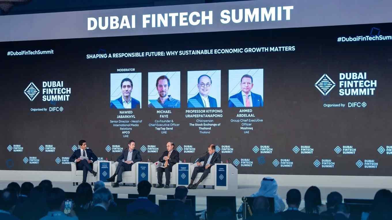 Panel discussion at the Dubai FinTech Summit with four industry leaders on stage discussing sustainable economic growth. A large screen behind them displays the session title, speaker profiles, and Dubai FinTech Summit branding, with attendees seated in the audience.