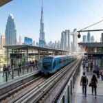Dubai Metro train arriving at a modern station with Burj Khalifa and Downtown Dubai skyline in the background.