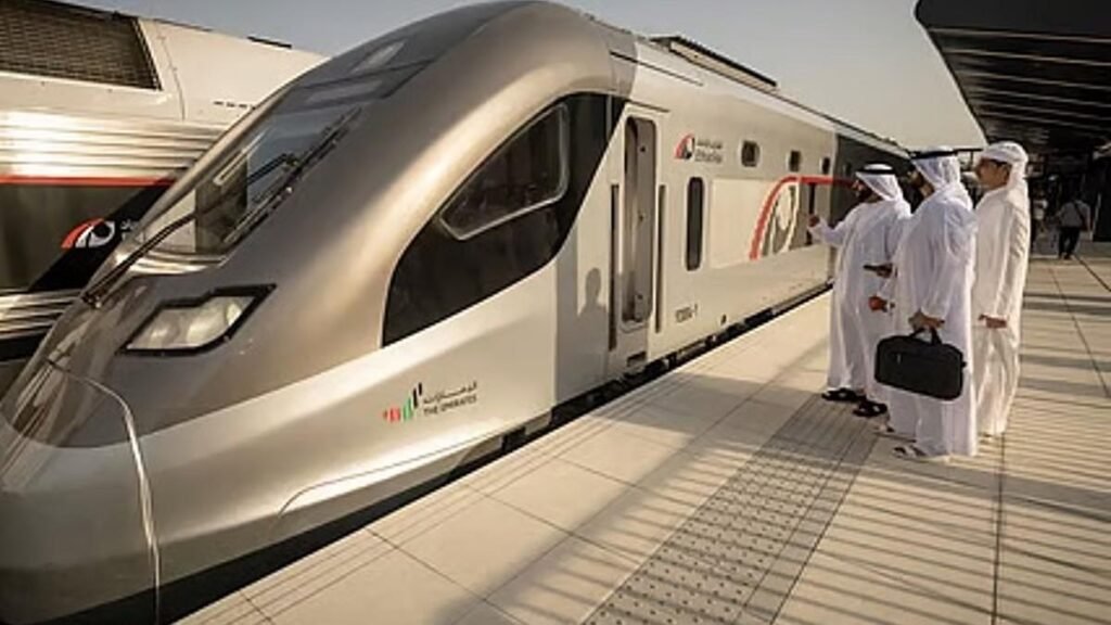 Etihad Rail passenger train stopped at a station platform as passengers in traditional Emirati clothing prepare to board.
