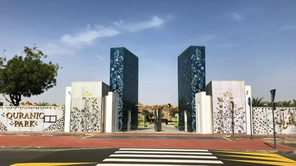 Main entrance to Quranic Park Dubai in Al Khawaneej with decorative floral gates, modern architecture, landscaped surroundings, and the park entrance sign under a clear blue sky.