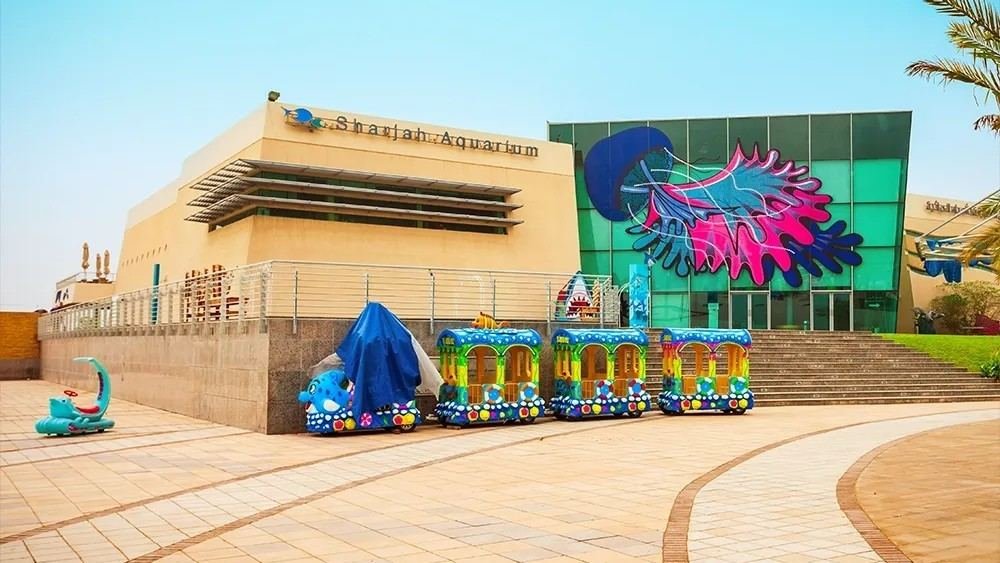 Exterior of Sharjah Aquarium in Al Khan, featuring the main entrance, colourful marine mural, and family friendly forecourt.