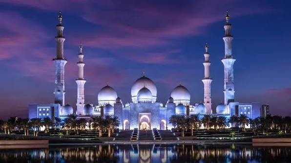 Sheikh Zayed Grand Mosque illuminated at dusk in Abu Dhabi, with its white marble domes, towering minarets, and reflections creating one of the city's most iconic free attractions.