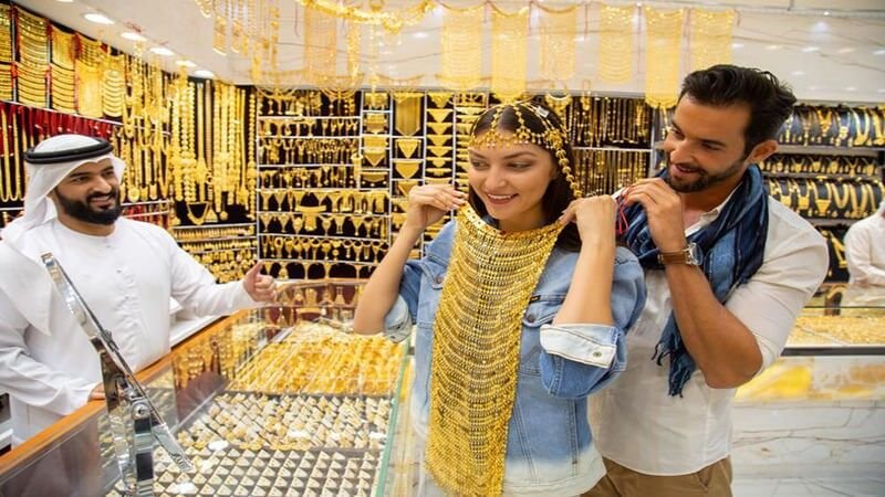 Tourists trying on traditional gold jewelry inside a Dubai Gold Souk jewellery store.