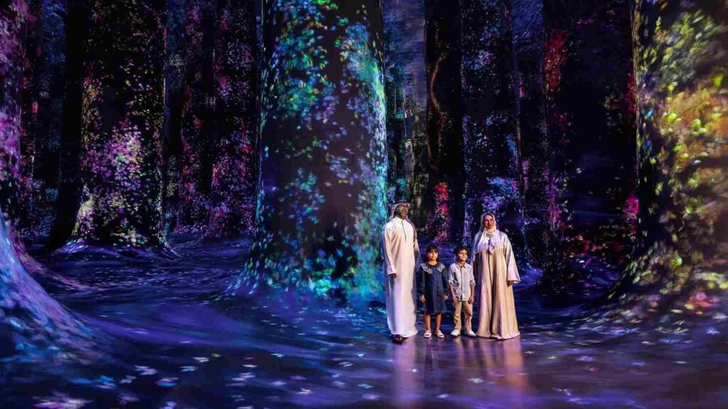 Family standing inside TeamLab Phenomena Abu Dhabi's immersive forest installation, surrounded by colourful digital projections of flowers and light covering the walls and floor.