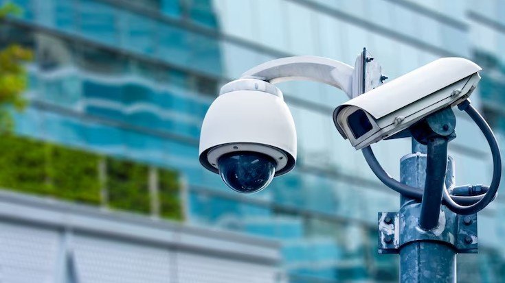 Close up of dome and bullet CCTV surveillance cameras mounted on a pole outside a modern glass building.
