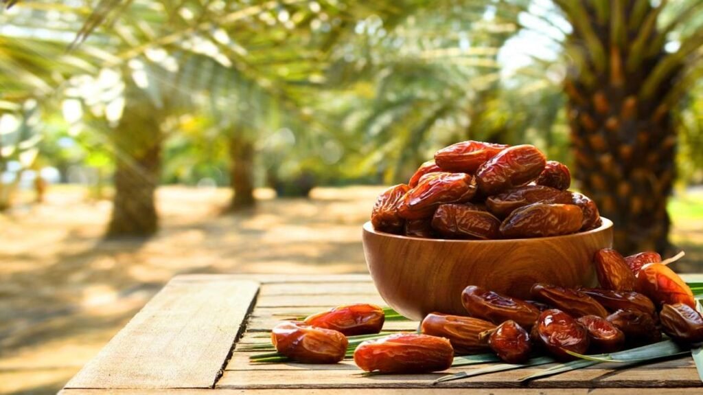 Fresh dates displayed in a wooden bowl on a table with date palm trees in an Abu Dhabi plantation, highlighting the UAE's rich date farming heritage.