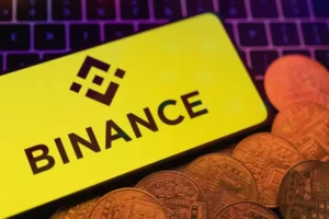 Smartphone with displayed Binance logo and representation of cryptocurrencies are placed on a keyboard