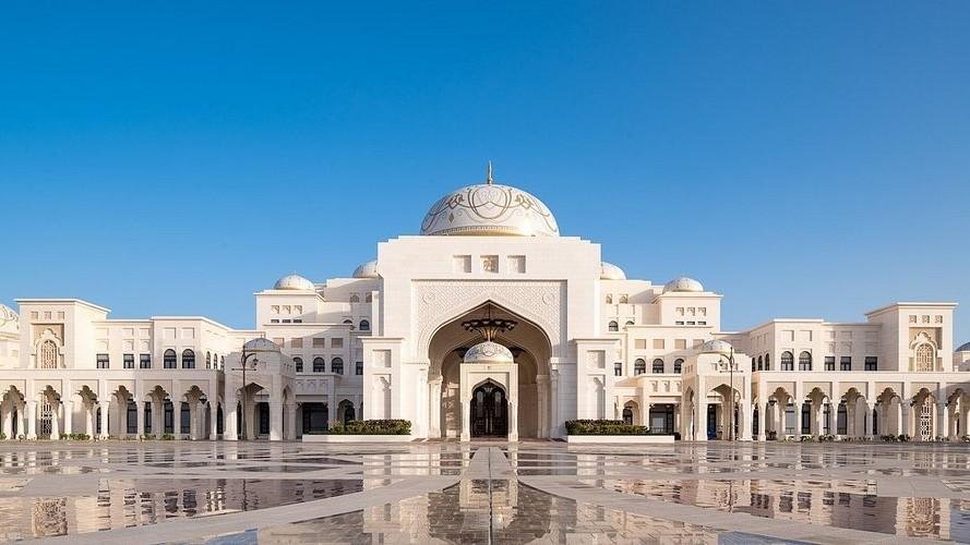 The exterior of Qasr Al Watan in Abu Dhabi, showing the white granite façade, central dome, grand entrance, and reflective courtyard beneath a clear blue sky.