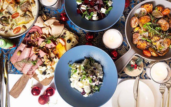 Overhead view of dishes served at The 3 Crystals at Mövenpick Downtown Dubai, featuring roasted vegetables, cheese salad, charcuterie, and festive table decorations.