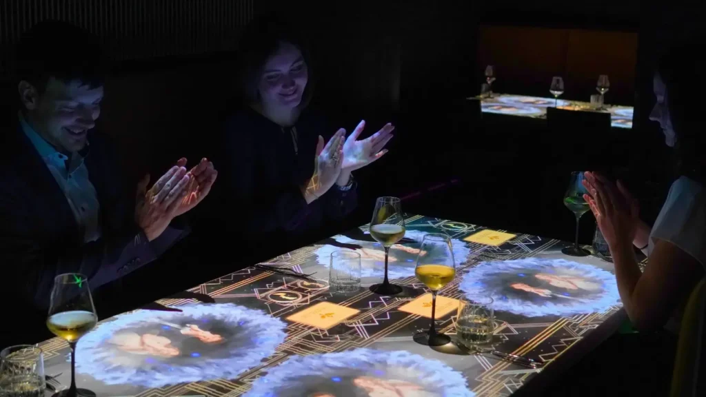 Guests sit around an illuminated dining table as digital projections and visual effects create an immersive magic themed dining experience.