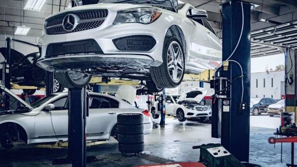 Luxury vehicles being serviced inside a UAE auto repair workshop, with several cars raised on hydraulic lifts while technicians carry out maintenance and inspection wor